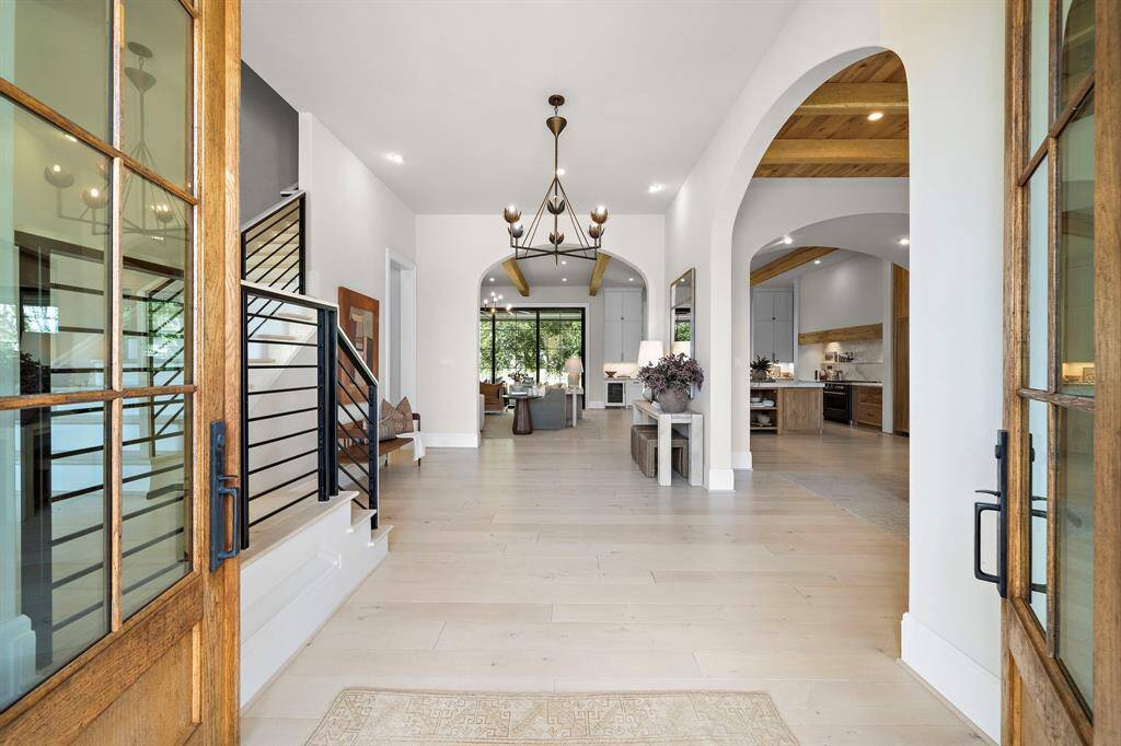 This gorgeous entryway features Certified French White Oak flooring, high ceilings, and elegant chandelier. Arched doorways lead to an open living area and a formal dining room with a wood accented ceiling.
