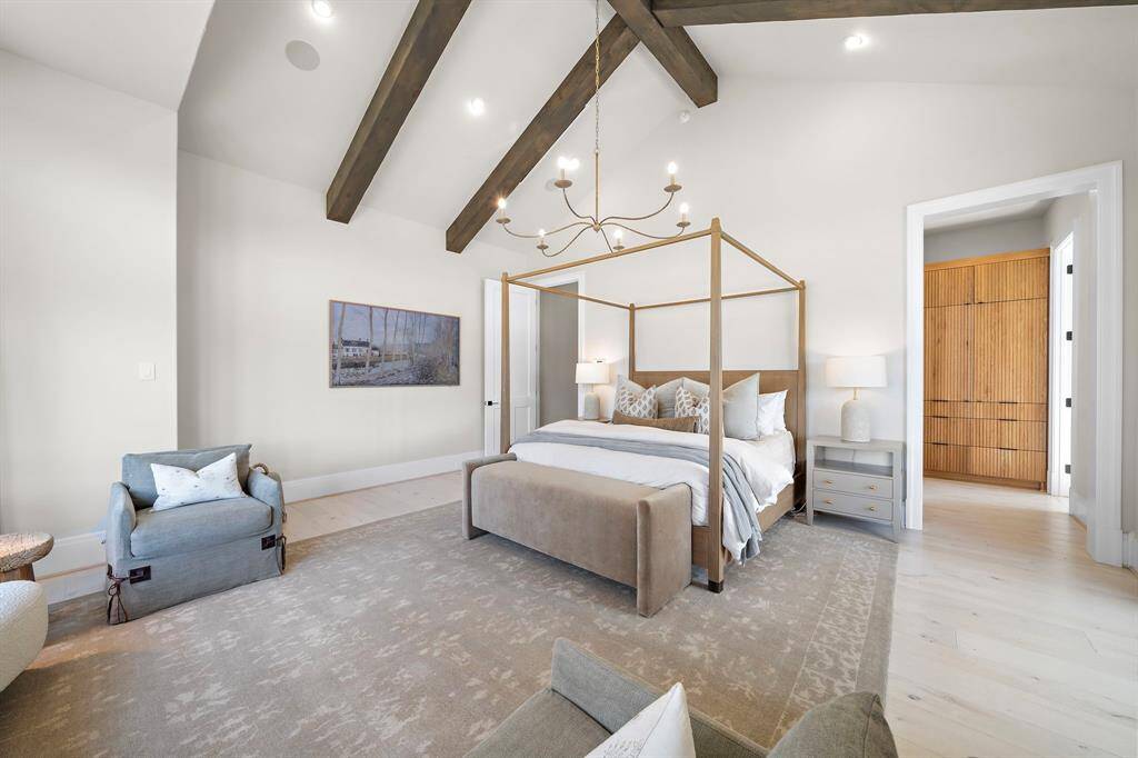 The primary bedroom is accessed through a private hallway and features spacious bedroom with a seating area, vaulted ceilings, designer chandelier, and accented with wood beams.