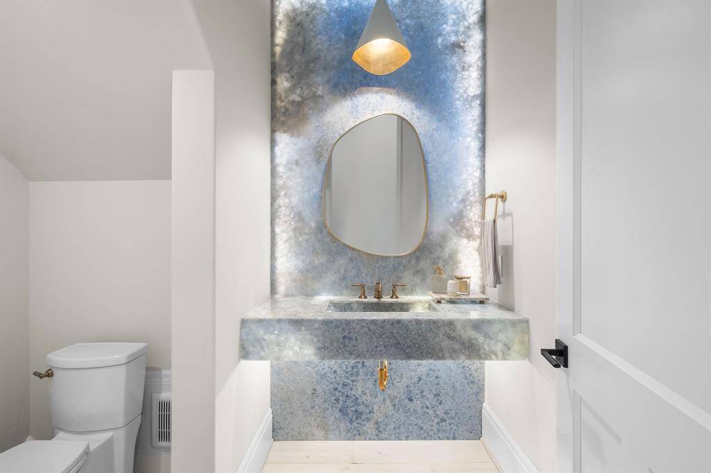 The guest bathroom features a gorgeous Onyx focal wall with back lighting highlighting how truly stunning this piece is. This wall is complimented beautifully with gold plumbing fixtures.