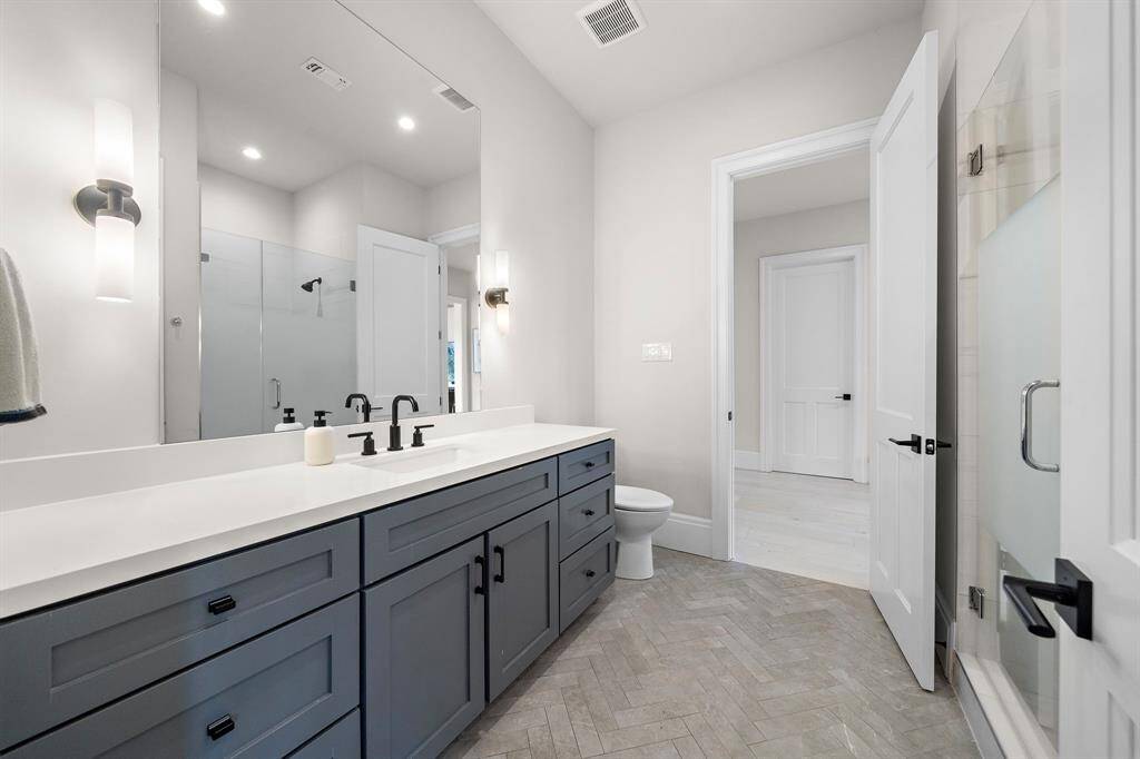 Upstairs bathroom serving both bedroom three and game room. Added details include a walk-in shower with a glass door with privacy shading, and a herringbone patterned floor.