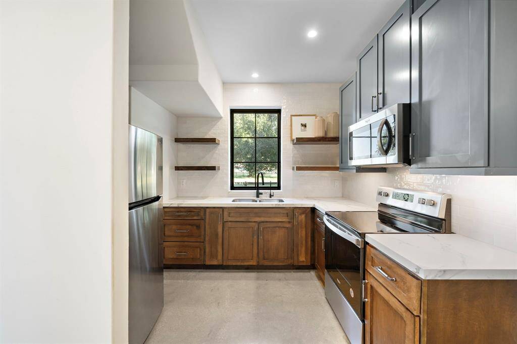 Casita kitchen with a sink, oven, microwave, and refrigerator.  Plenty of counter space as well as storage cabinets and floating shelves for dish display.