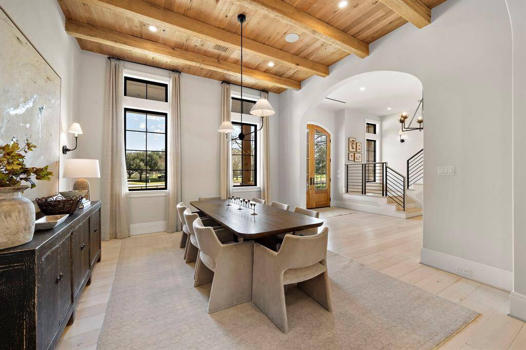 Elegant dining room showcases a designer pendant, reclaimed wood beams, and ample natural light from tall windows.