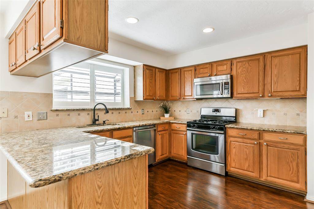 Continue into the U-shaped kitchen to find ample cabinetry topped with granite countertops, a ceramic tile backsplash, recessed lighting, and stainless appliances, including a gas cooktop, single oven, vent hood microwave, and concealed control dishwasher.