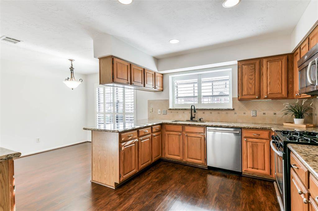 Continue into the U-shaped kitchen to find ample cabinetry topped with granite countertops, a ceramic tile backsplash, recessed lighting, and stainless appliances, including a gas cooktop, single oven, vent hood microwave, and concealed control dishwasher.