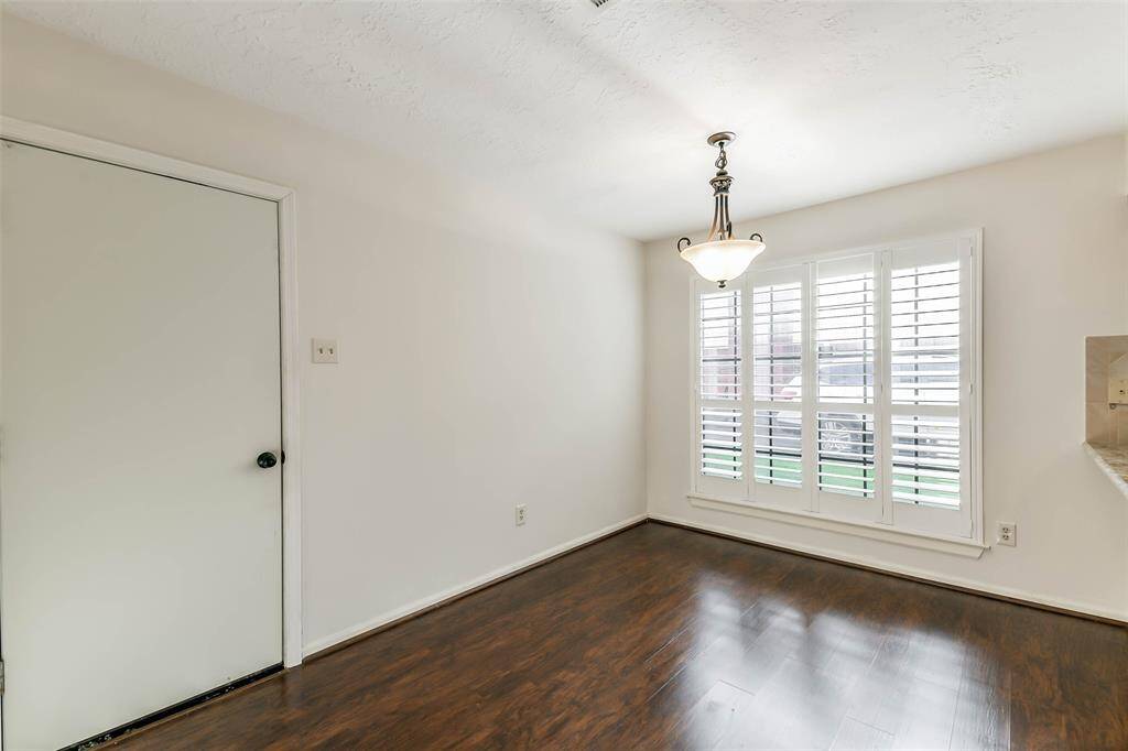 Situated between the garage entrance and the kitchen, you'll find a casual breakfast area with luxury vinyl plank floors, neutral paint, a side-facing window with plantation shutters, and a granite-top breakfast bar leading into the kitchen.