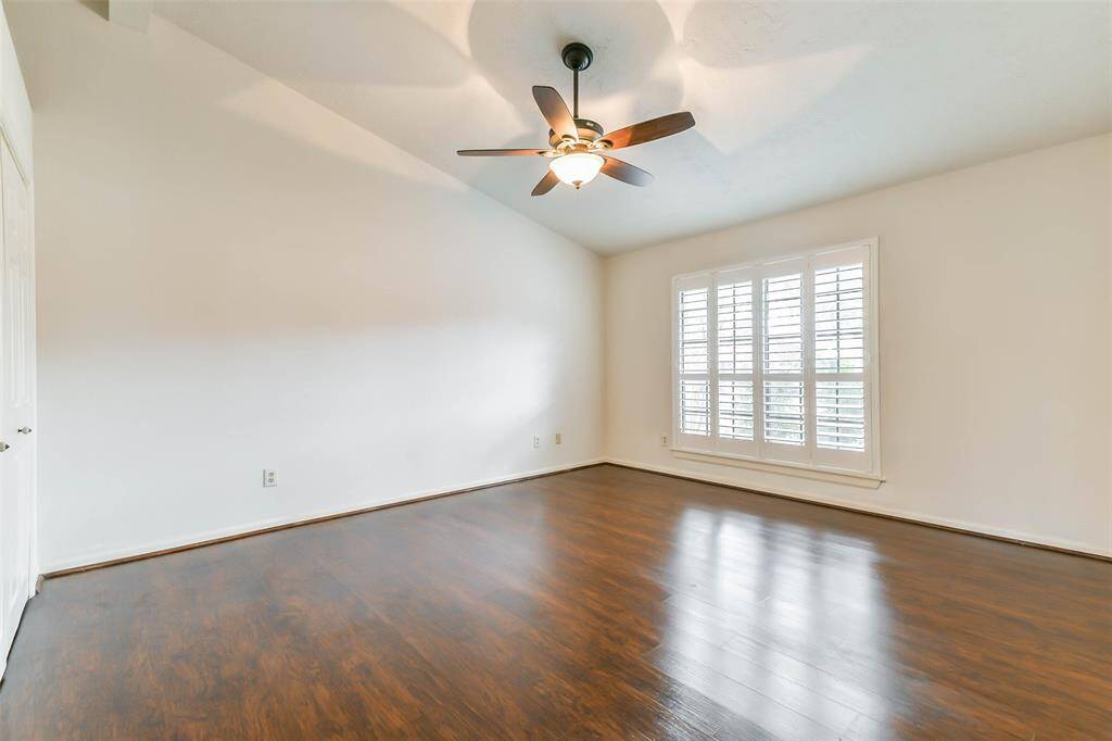 Escape to the first-floor owner's retreat to find a soaring vaulted ceiling with a lighted ceiling fan, neutral paint, luxury vinyl plank floors, an en suite bathroom, and a large window with plantation shutters and backyard views.