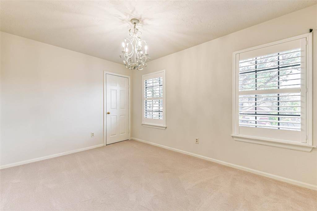 The first of three secondary bedrooms that are all located on the second floor features a lovely candelabra chandelier, neutral paint, plush new carpet, a walk-in closet, and a pair of front-facing windows dressed with plantation shutters.