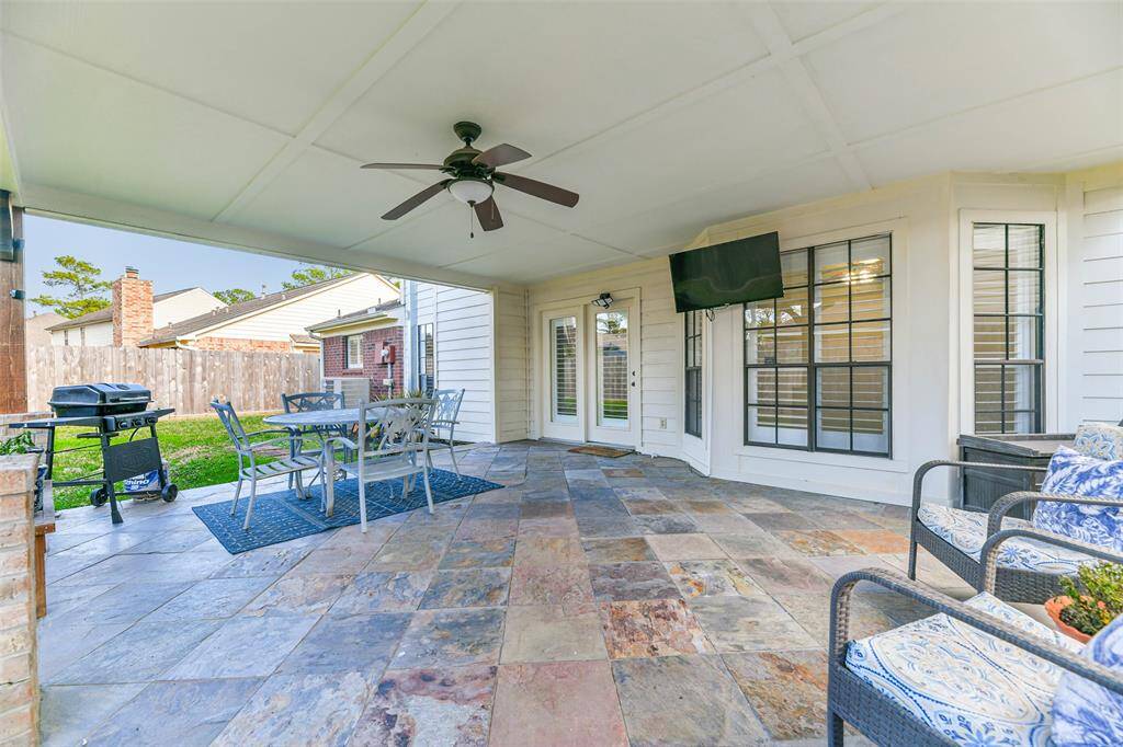 Step outdoors through a full panel glass door in the family room to this spacious and breezy covered back patio with slate tile floors, a lighted ceiling fan, and views of the lush fenced backyard.