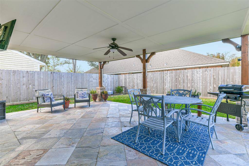 Step outdoors through a full panel glass door in the family room to this spacious and breezy covered back patio with slate tile floors, a lighted ceiling fan, and views of the lush fenced backyard.