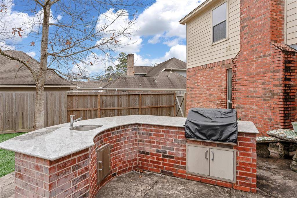 Outdoor kitchen area features an oversized counter top, sink, gas grill  & bar area.