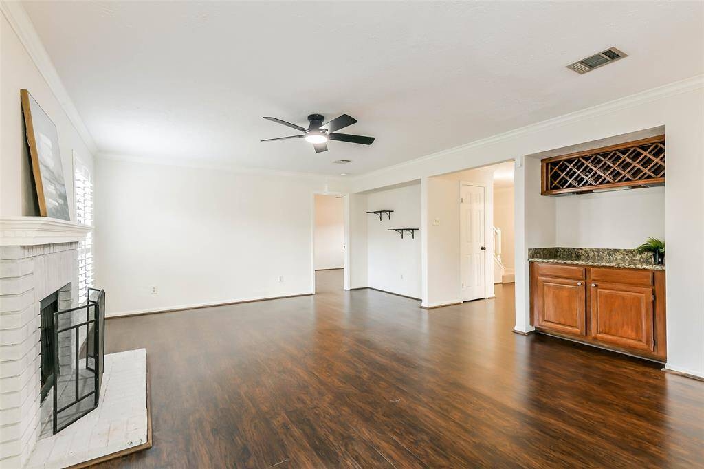 The foyer spills into this extra-spacious family room that boasts a charming painted brick fireplace with gas connections, a modern lighted ceiling fan, luxury vinyl plank floors, neutral paint, and a built-in bar with granite countertops and bottle storage.