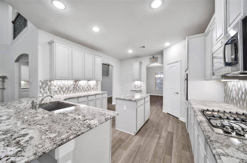 Large open kitchen featuring tall cabinetry, soft close drawers, granite countertops, stainless steel appliances, and a stylish mosaic backsplash