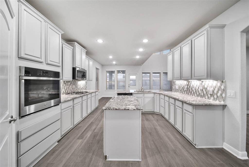 Large open kitchen featuring tall cabinetry, soft close drawers, granite countertops, stainless steel appliances, and a stylish mosaic backsplash