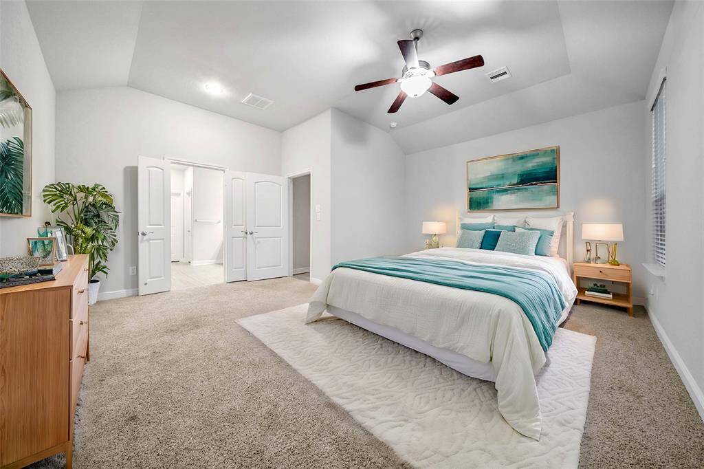 The primary suite offers a well-lit bedroom featuring high ceilings, plush carpeting, a ceiling fan, and multiple windows for natural light.