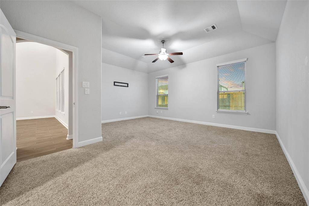 The primary suite offers a well-lit bedroom featuring high ceilings, plush carpeting, a ceiling fan, and multiple windows for natural light.