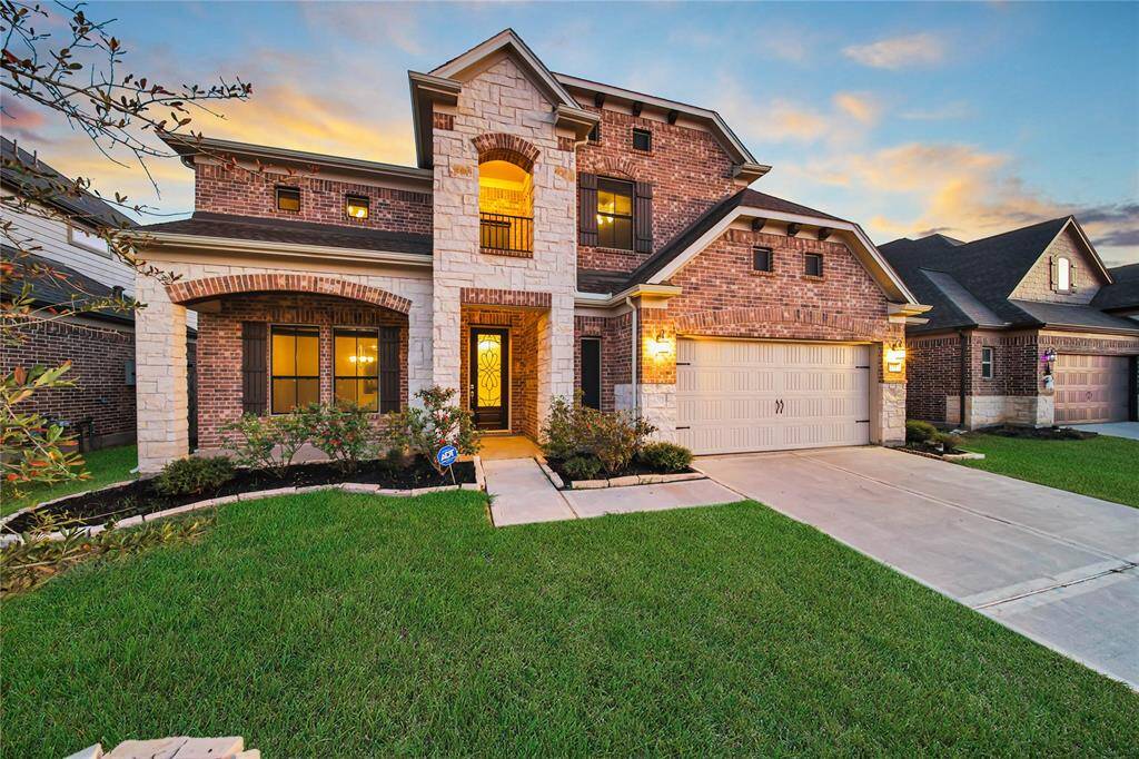 This is a two-story brick home with a well-maintained lawn, an arched entryway, and an oversized two-car garage.
