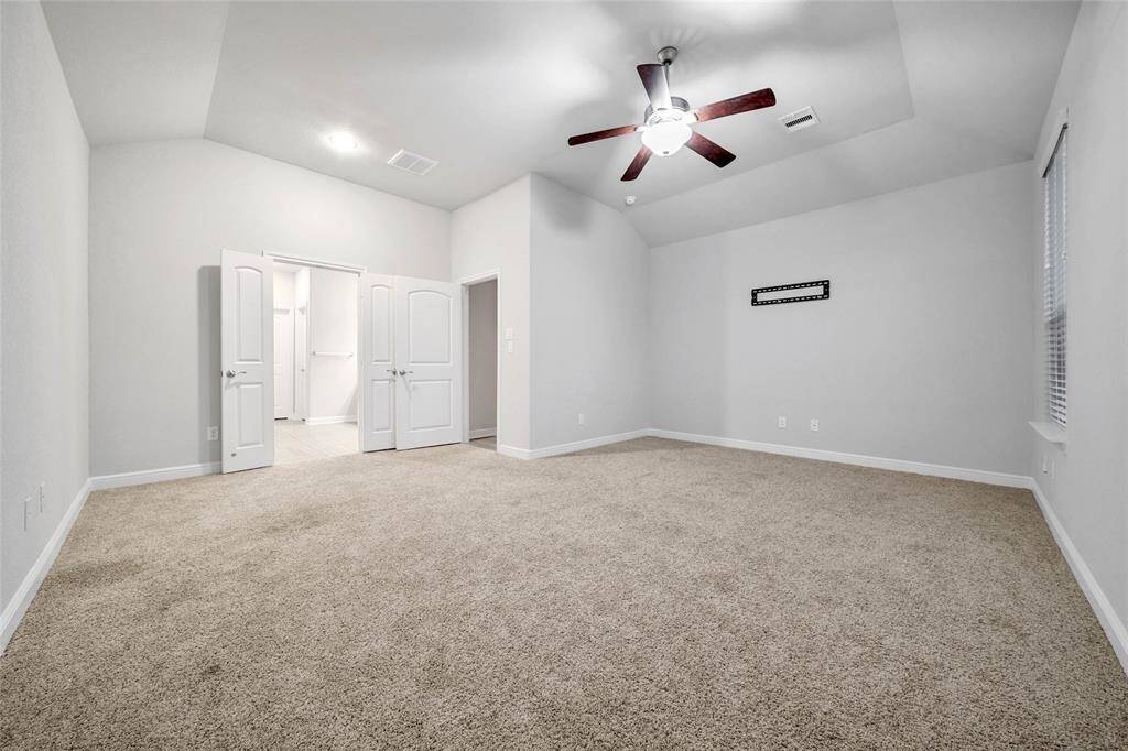 The primary suite offers a well-lit bedroom featuring high ceilings, plush carpeting, a ceiling fan, and multiple windows for natural light.