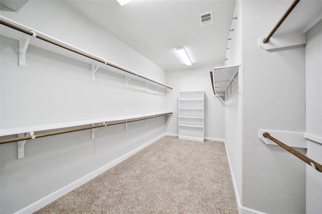 The primary closet offers an abundance of space with ample shelving and hanging racks, featuring a neutral color scheme and plush carpeting.