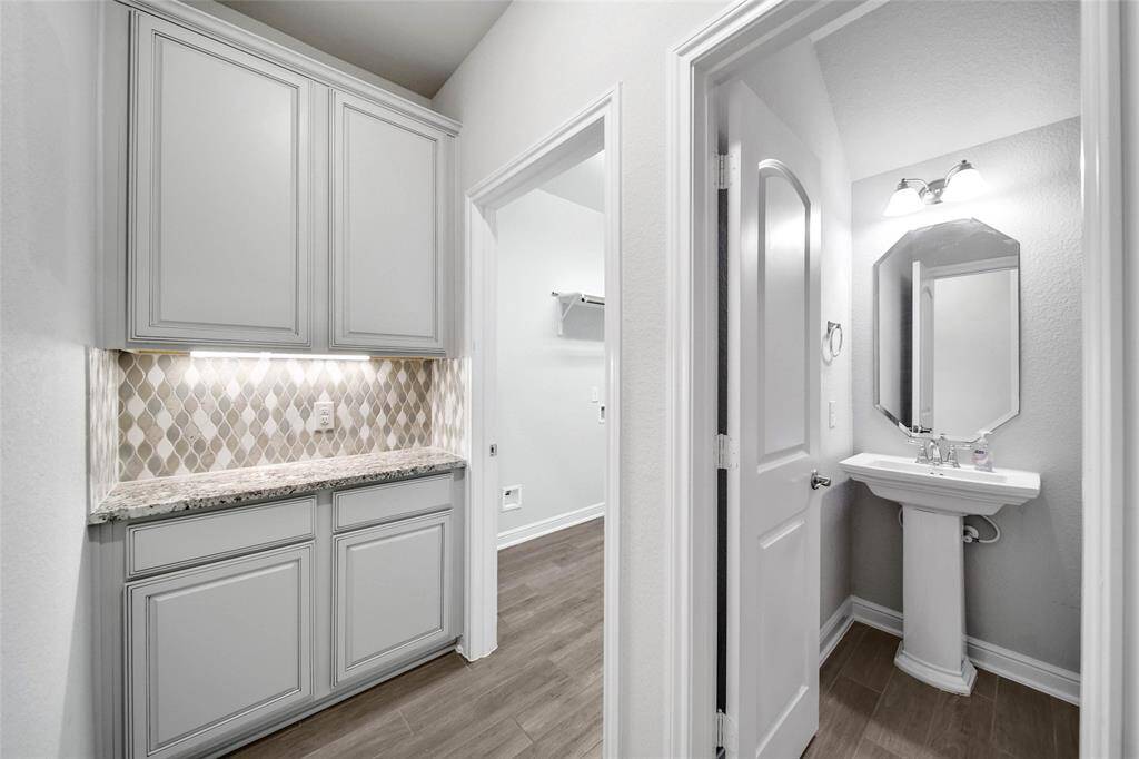 built-in cabinets with a stylish backsplash, ideal for extra storage or a dry bar area. To the right is a neatly presented half bathroom with a pedestal sink and a framed mirror above it.