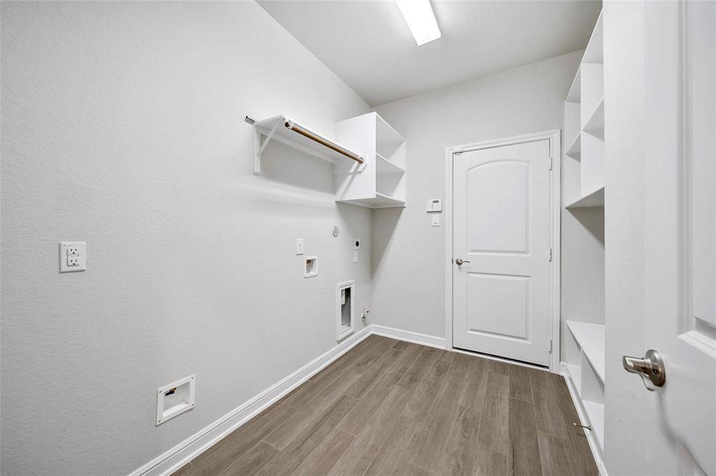Well-lit, modern laundry room with built-in shelving, wood-look flooring, and a convenient hanging rod. Don't miss the extra water line ready for a second in home refrigerator.