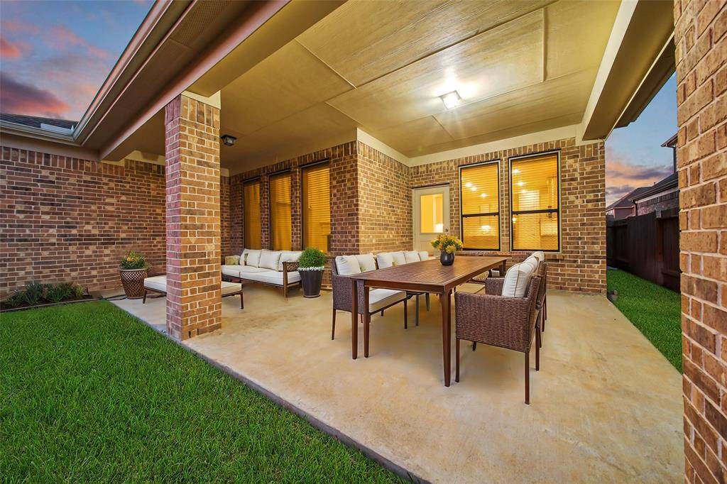 This is a spacious, covered patio area with elegant brickwork. This patio can easily fit an outdoor dining set and a comfortable seating area, perfect for entertaining or relaxing. The well-maintained lawn adds a touch of greenery, and the space benefits from outdoor lighting, allowing for evening enjoyment.