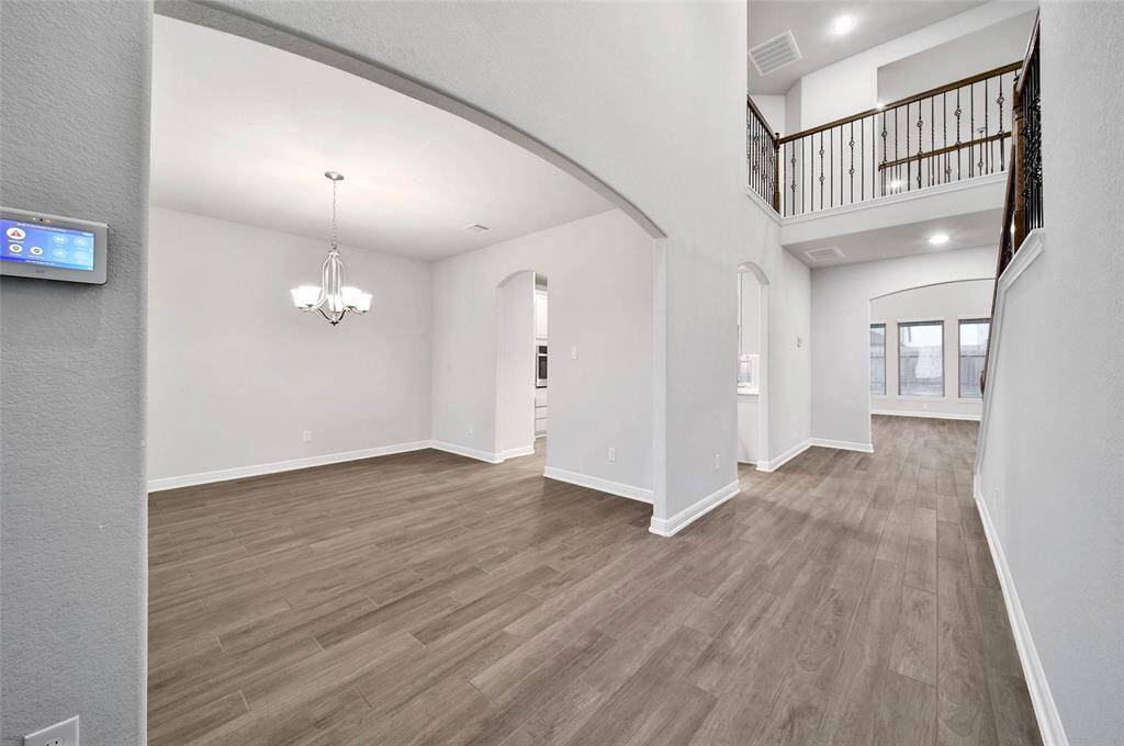 Bright Foyer with elegant wood look tile flooring, a high ceiling, an archway leading to the office, and an upstairs balcony overlooking the space. It is well-lit with natural light from the windows.