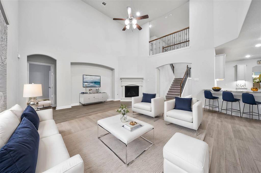This is a spacious, modern living room with high ceilings and ample natural light. It features a cozy fireplace, an open staircase leading to a second level, and a seamless transition to a dining area with a breakfast bar.