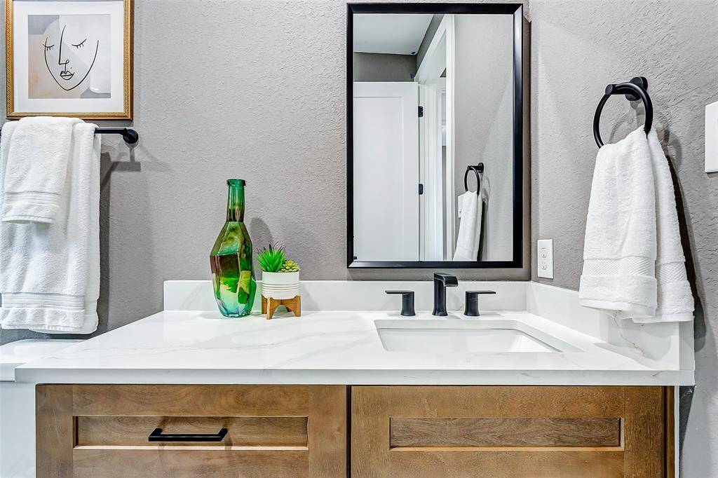 Elegant bathroom with a wooden vanity, modern black fixtures, quartz countertop, and a sleek framed mirror for a sophisticated touch.
