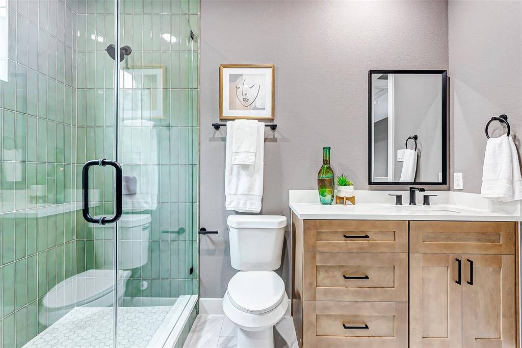 Experience modern elegance in this bathroom with a sleek glass shower, chic green tiles, a wood-accented vanity, and bold black fixtures.