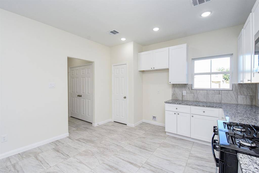 A modern kitchen with white cabinetry, granite countertops, and stainless steel appliances, featuring tile flooring and neutral color tones.