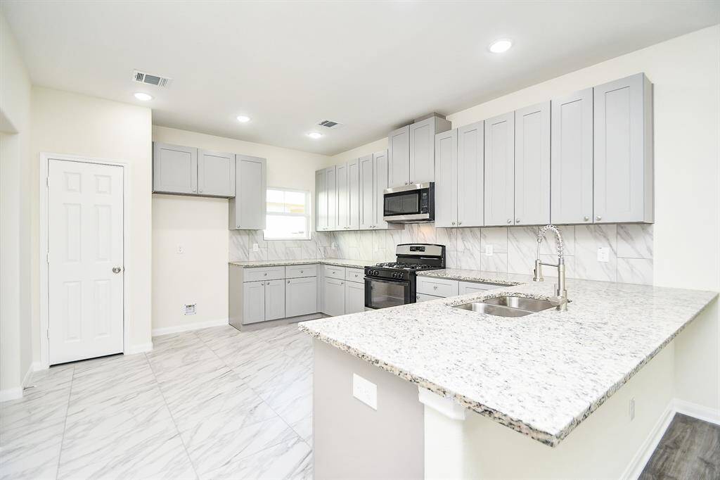 A modern kitchen with white cabinetry, stainless steel appliances, marble backsplash, and a large island with granite countertops.