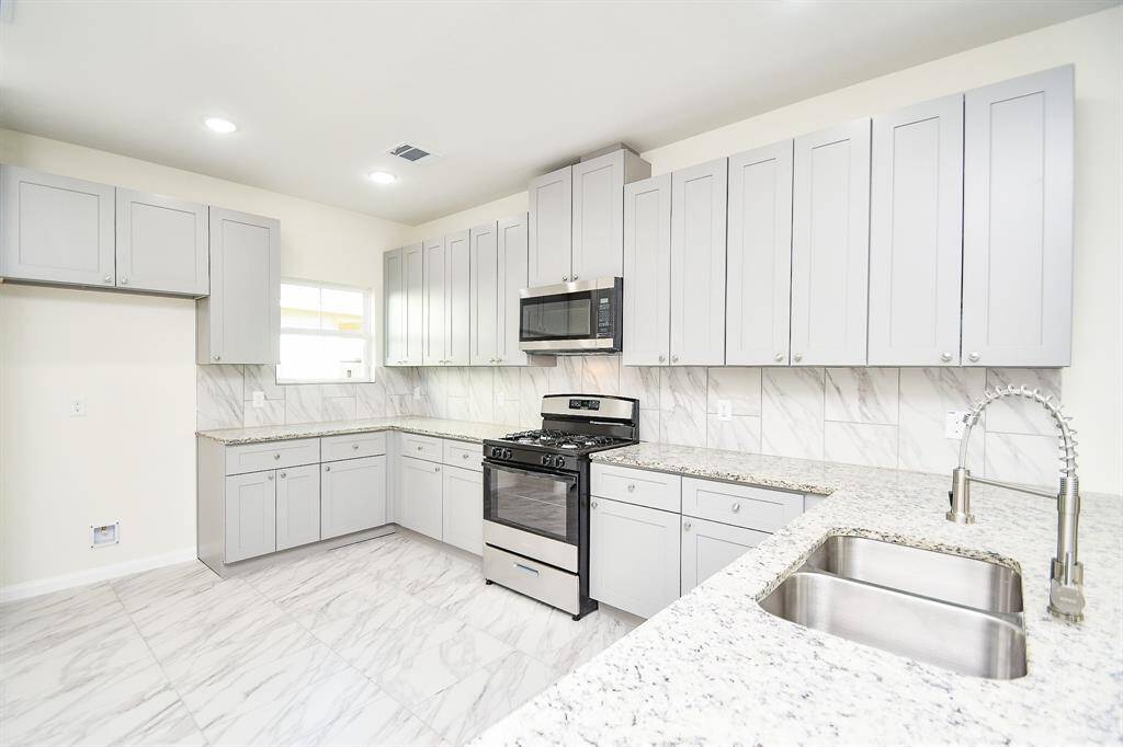 Modern kitchen with white cabinets, stainless steel appliances, marble backsplash, and granite countertops. Bright, clean, and unoccupied.