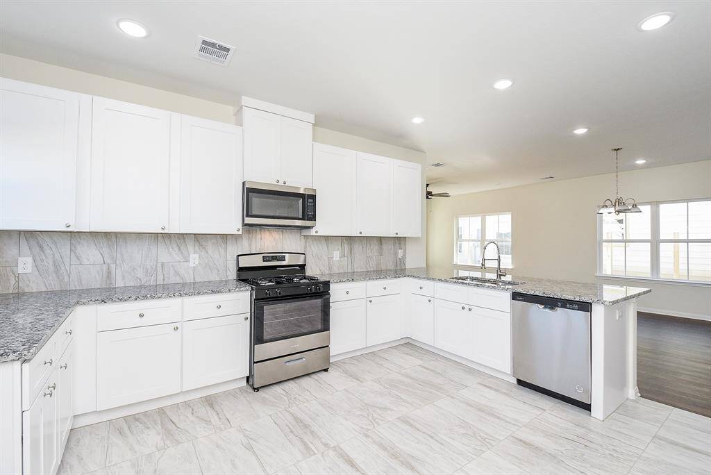 Modern kitchen with white cabinets, granite countertops, stainless steel appliances, and tiled floor. Bright, clean, and unoccupied space.