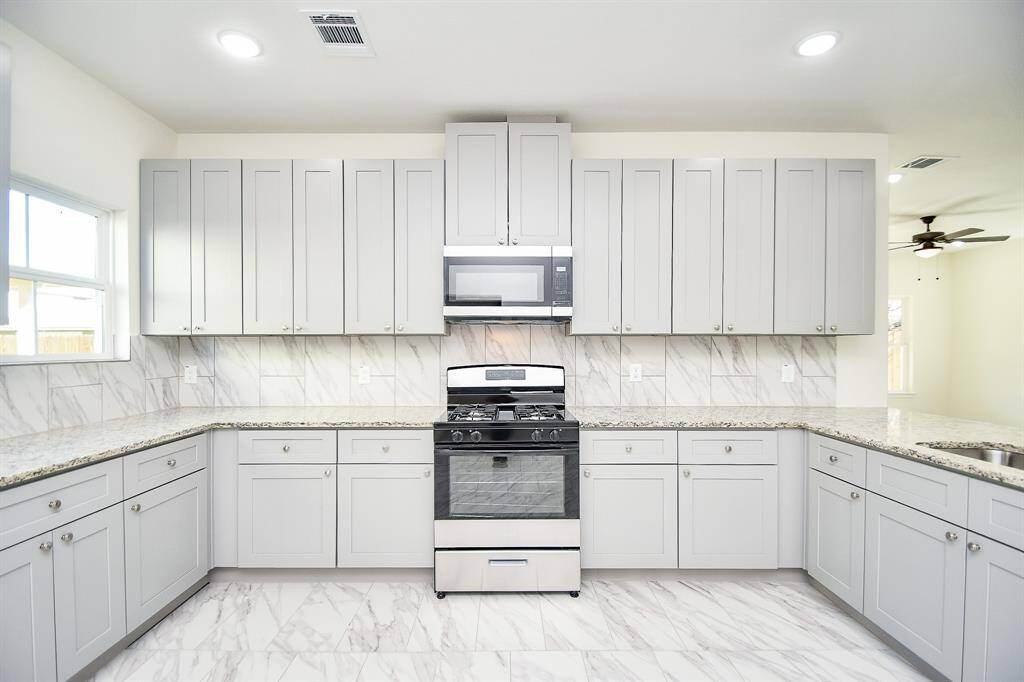 Modern kitchen with white marble countertops, grey cabinets, stainless steel appliances, and a ceiling fan. Bright, clean, and unoccupied.