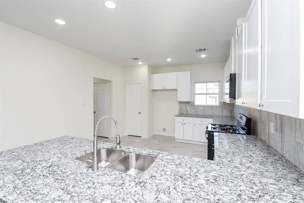 A modern, empty kitchen with white cabinets, stainless steel appliances, granite countertops, and tiled backsplash in a newly constructed home.