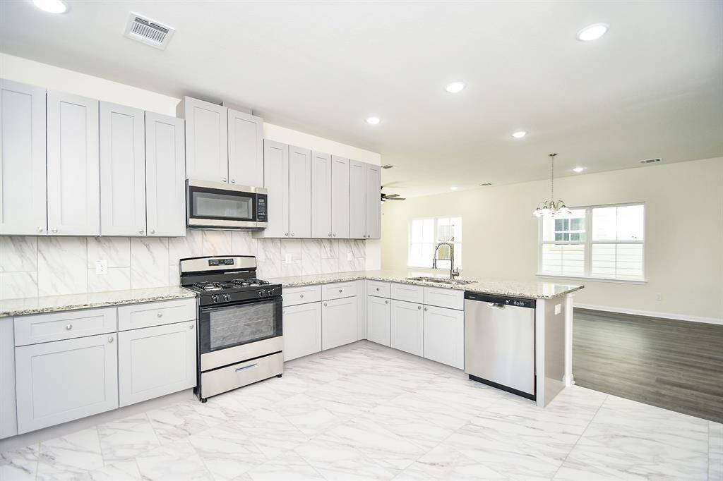 Modern kitchen with white cabinetry, stainless steel appliances, marble countertops, and recessed lighting. Bright, clean, and unoccupied space.