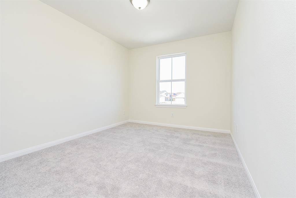 Empty room with beige walls, carpeted floor, one window, and a ceiling light fixture. It appears clean and vacant.