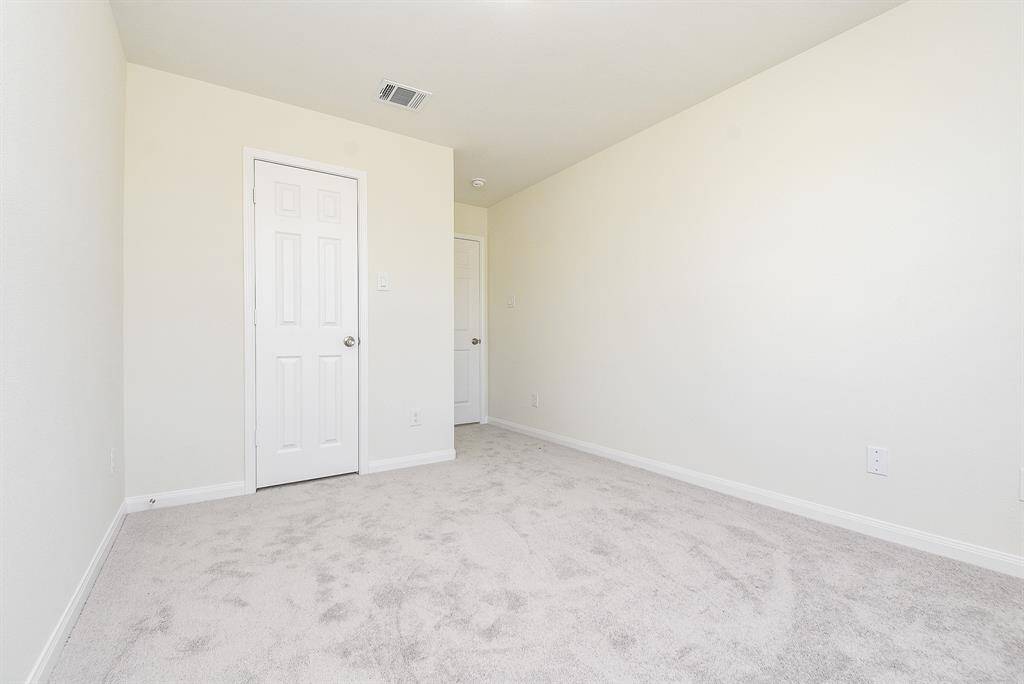 Empty room with beige walls, carpeted floor, white doors, and an air vent on the ceiling.