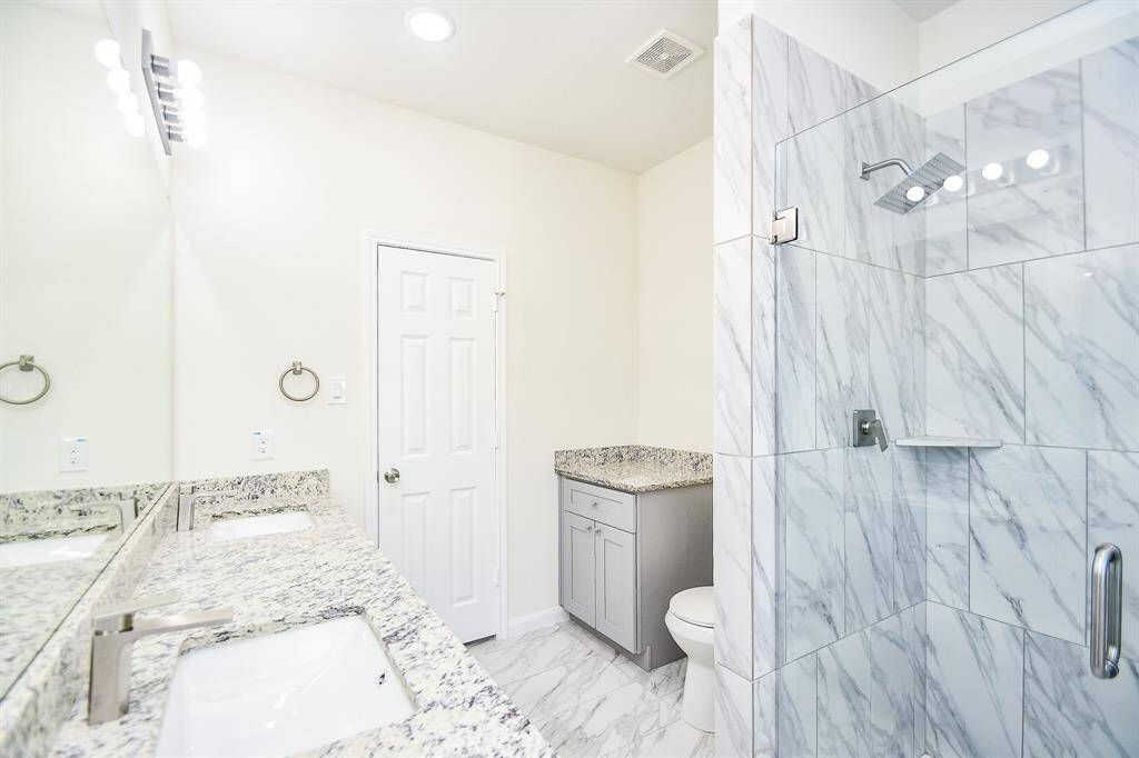 A modern bathroom with marble tiles, dual sinks, large mirror, glass shower enclosure, and white door. Clean and bright aesthetic.