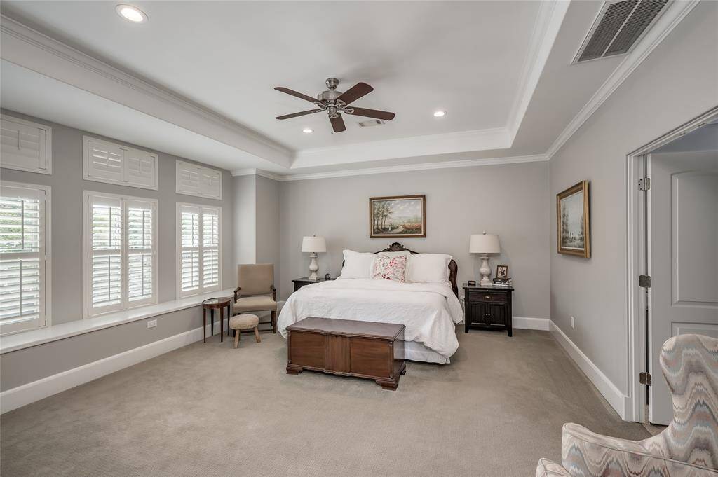 Generously sized primary bedroom features windows overlooking the front yard with plantation shutters, tray ceiling, crown moulding, and recessed lighting.