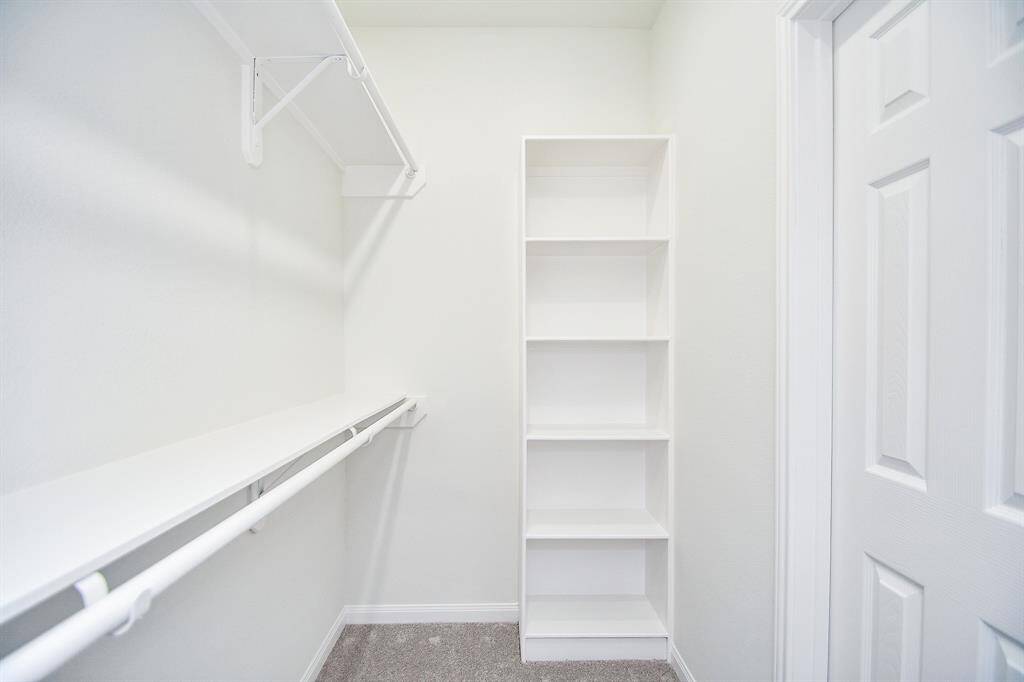 A small, empty walk-in closet with white walls, one shelf unit, and a hanging rod, illuminated by natural light.