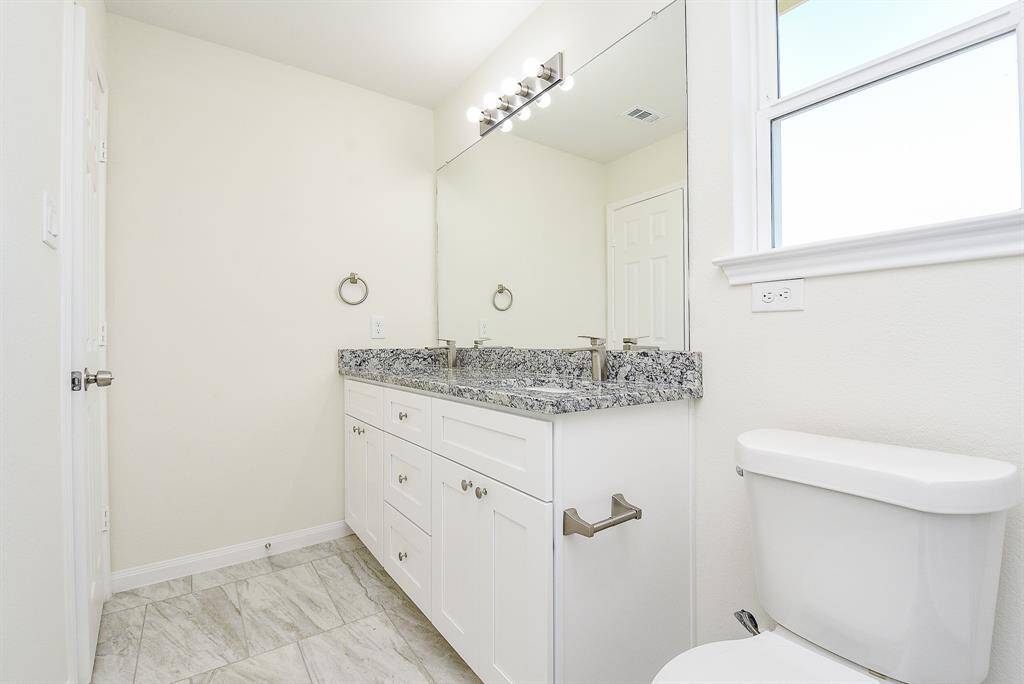 A clean, modern bathroom with a double vanity, large mirror, frosted window, and tiled floor.