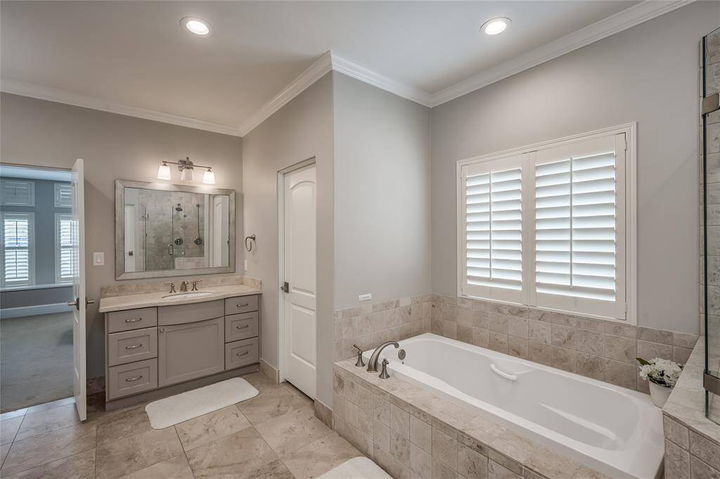 Spa-like master bathroom features double sinks with cabinetry below, window with plantation shutters overlooking the side yard, large soaking tub & walk-in shower.