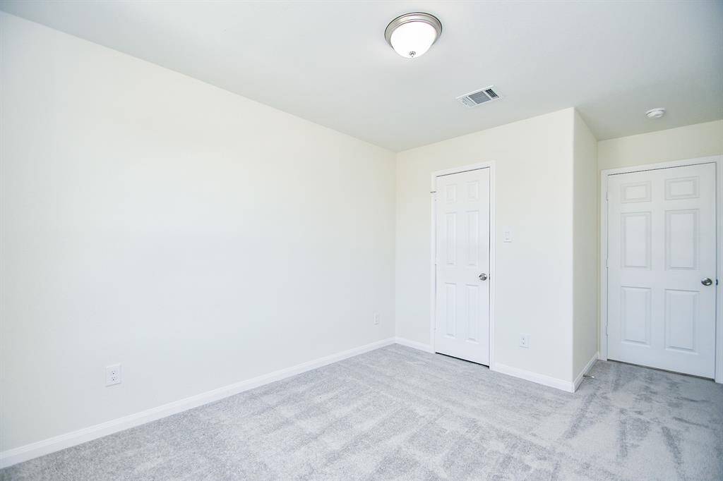 Empty room with white walls, gray carpet, two closed doors, and one ceiling light fixture.