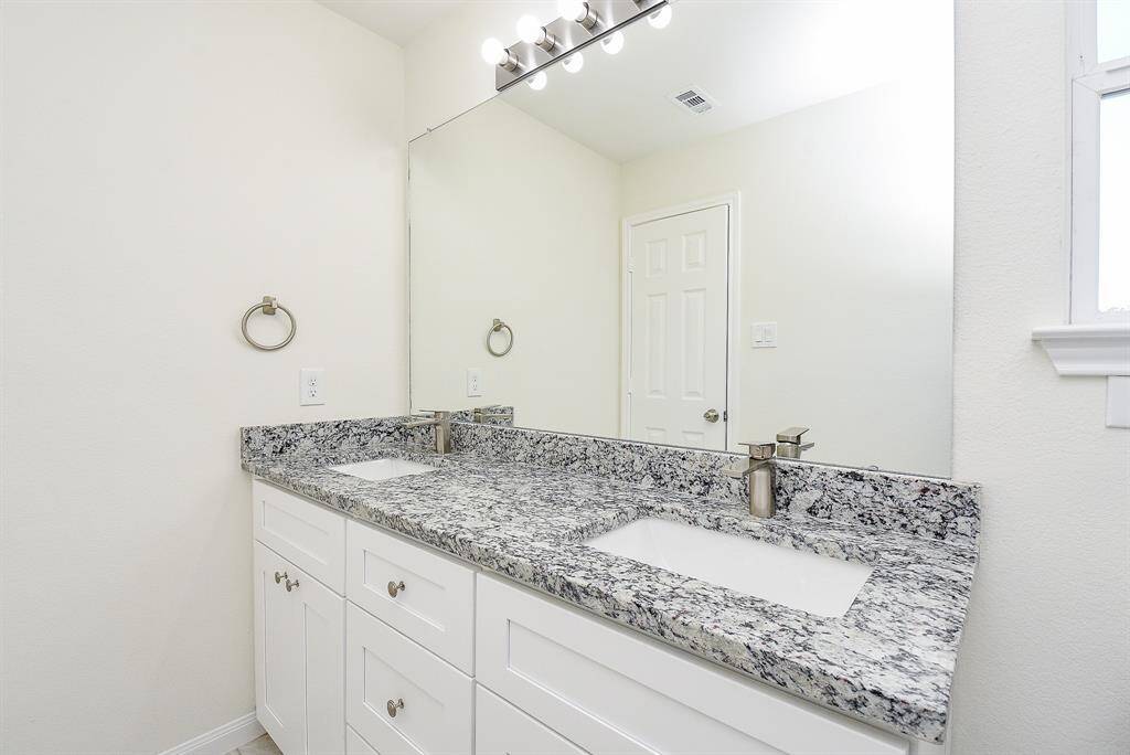 A clean, modern bathroom with a double vanity, granite countertops, large mirror, and bright lighting.