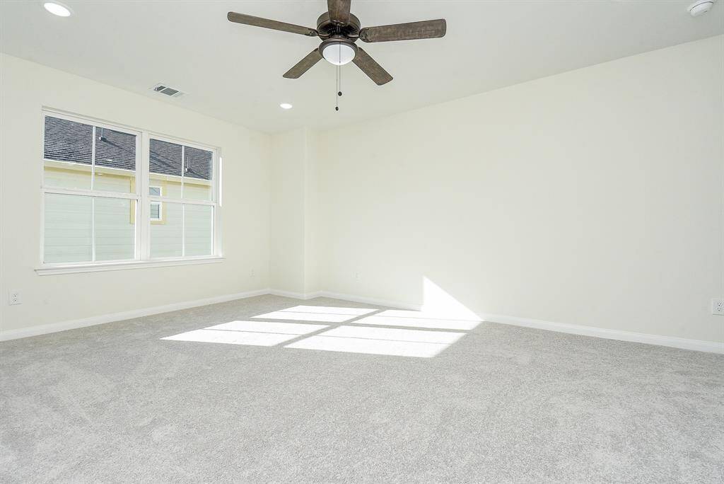 Empty room with carpeted floor, a ceiling fan, and sunlight casting shadows through a large window.