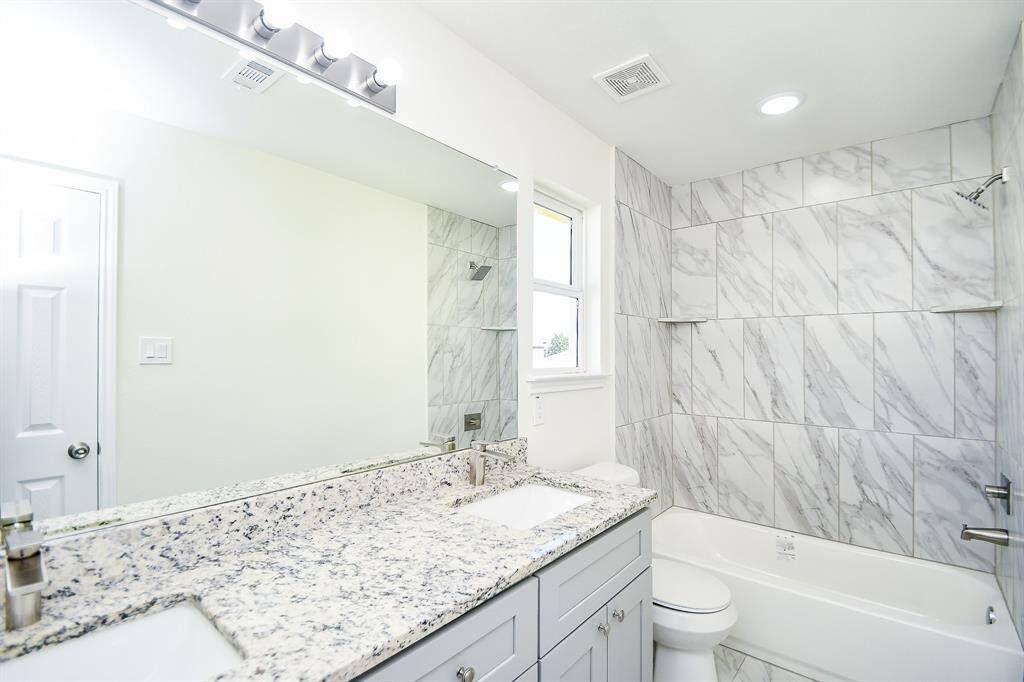 A clean, modern bathroom with marble tiles, a large mirror, granite countertop, undermount sink, and bright lighting.