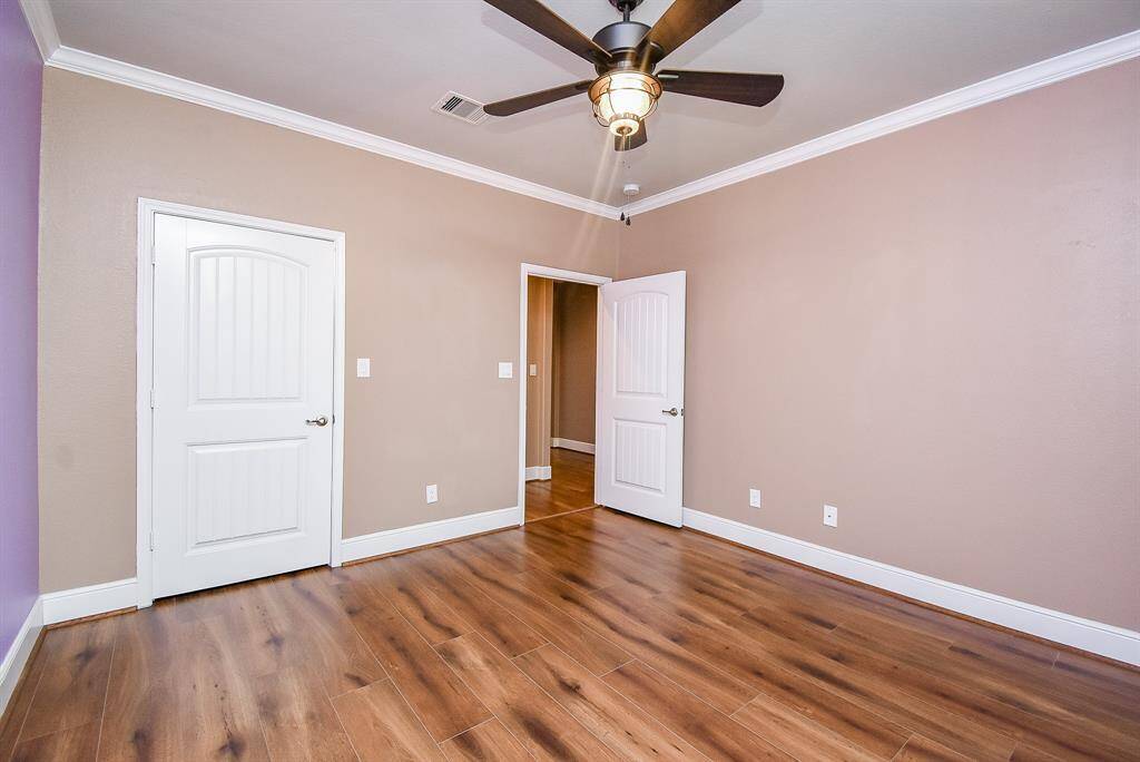 Charming secondary bedroom features durable luxury vinyl plank flooring, elegant plantation shutters, and custom trim and crown molding.