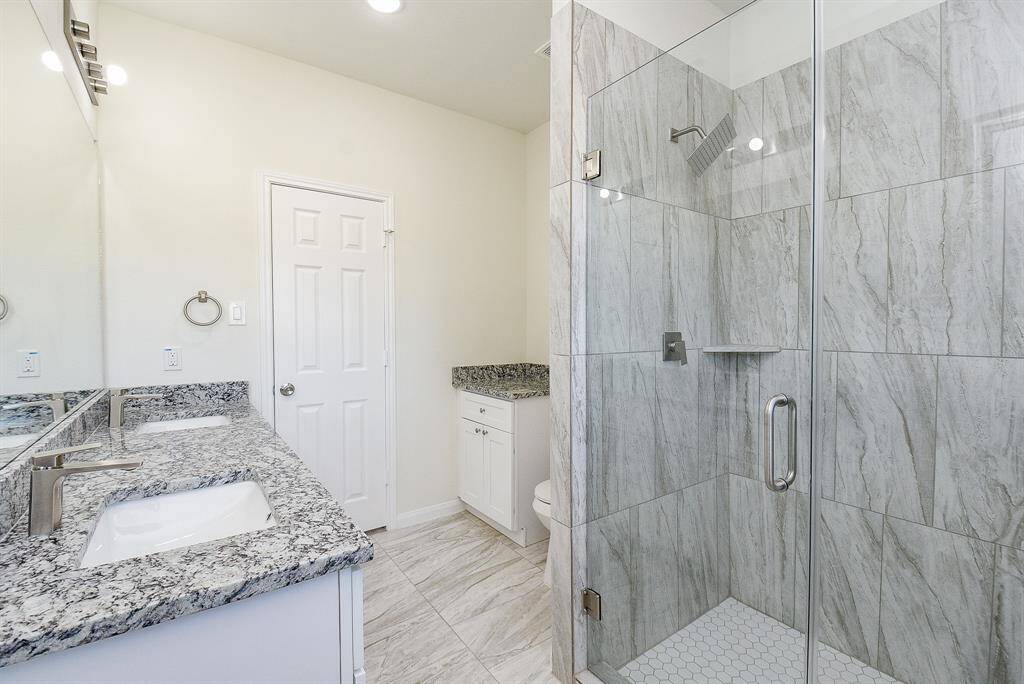 Modern bathroom with marble tiles, glass shower, white vanity with granite countertop, and large mirror. Clean and bright interior.