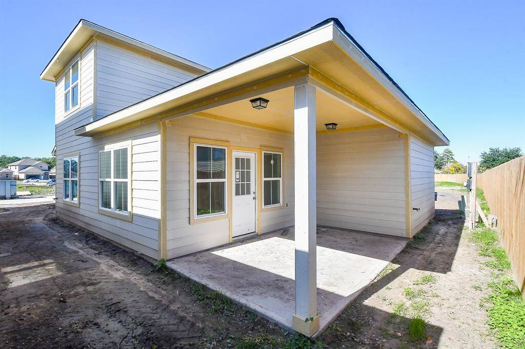 A newly constructed two-story house with a covered patio and an unfinished yard under a clear blue sky.
